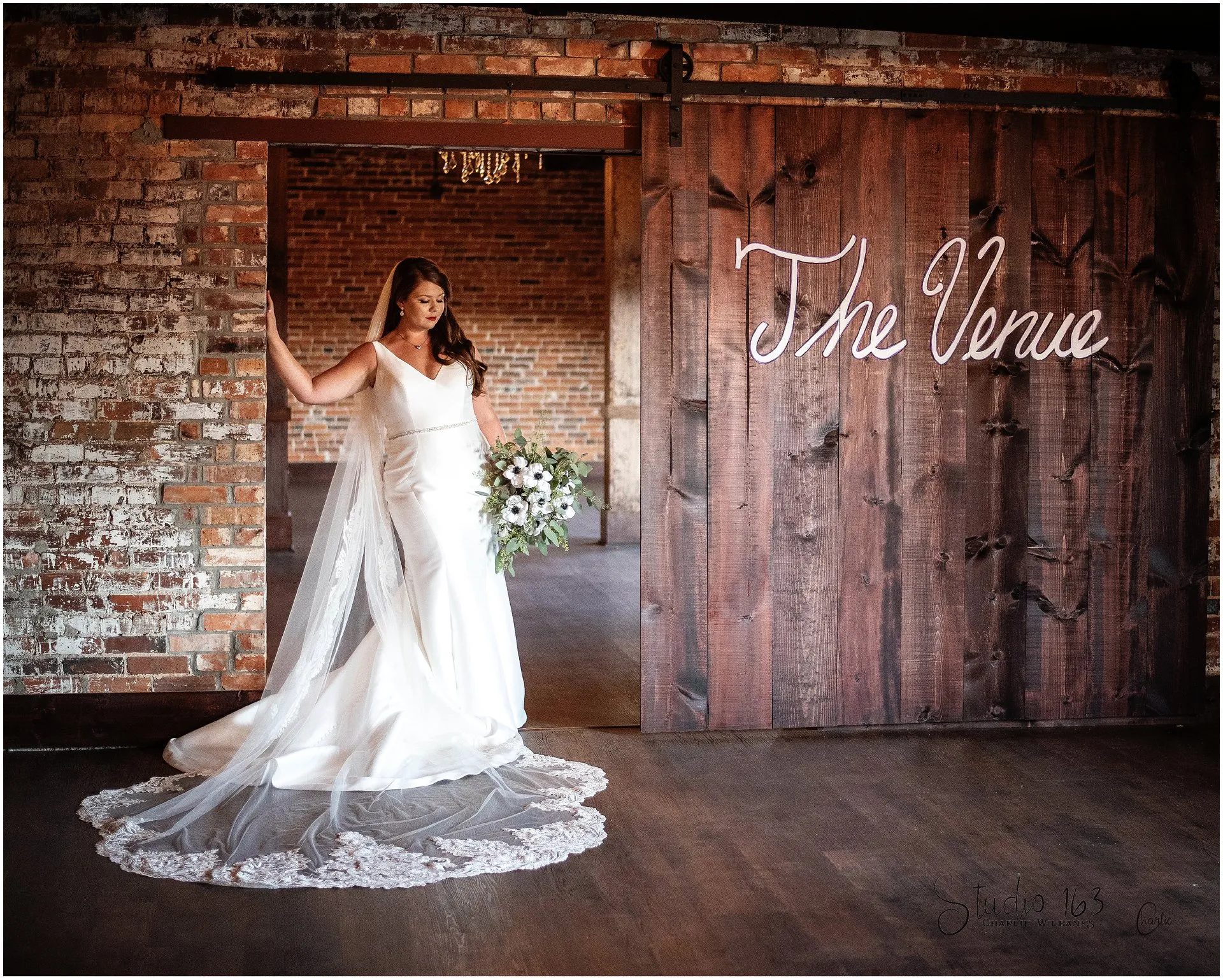A bride in a lace-trimmed gown beside The Cotton Loft’s timber doors and original brick