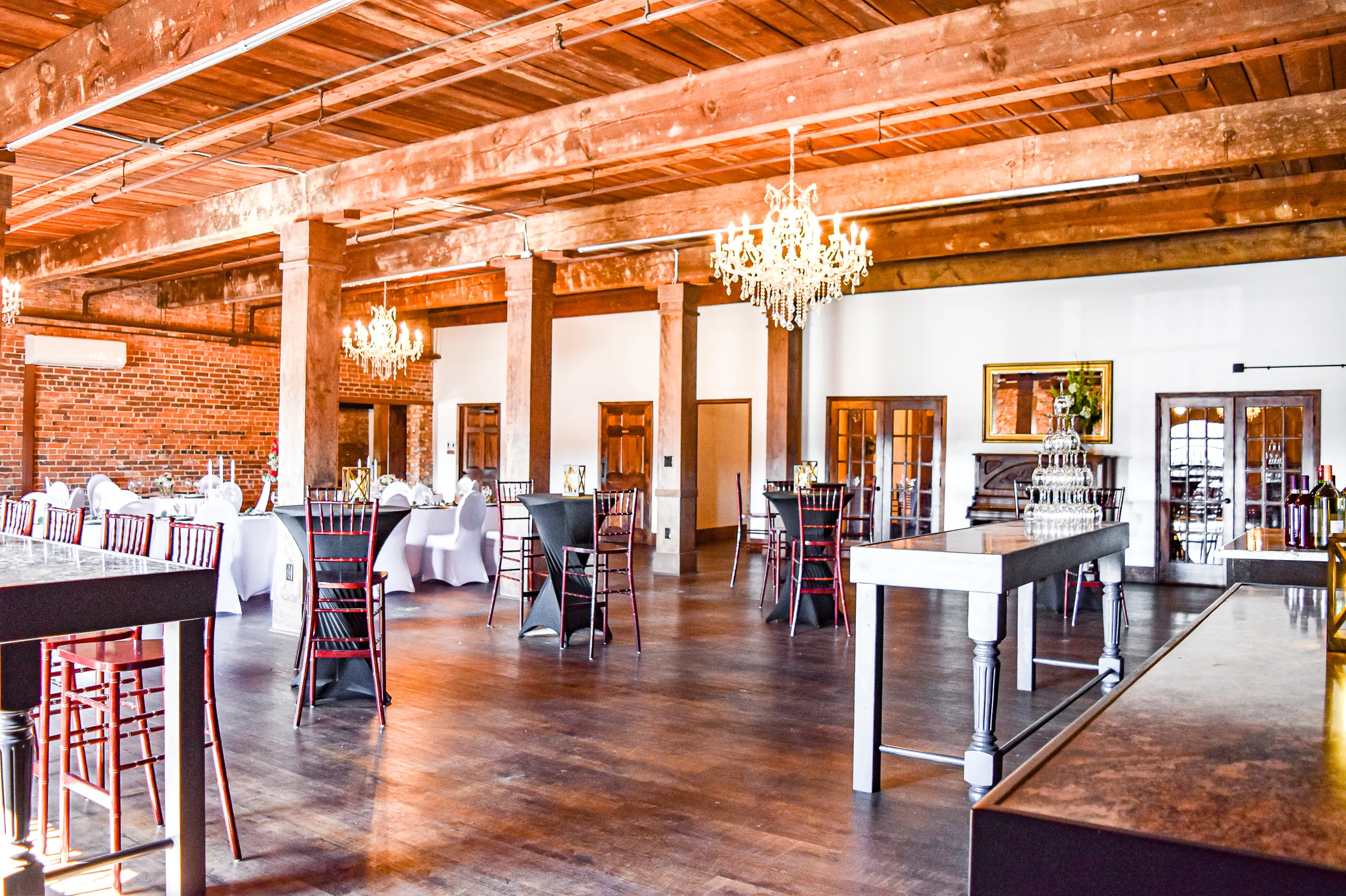 Open event floor and bar-height tables beneath chandeliers inside The Cotton Loft